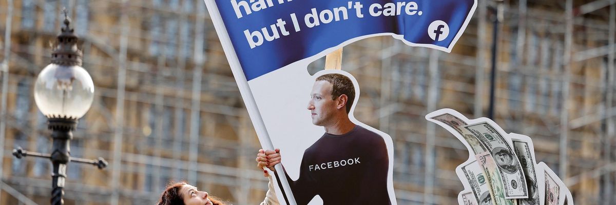 A demonstrator poses with an installation depicting Facebook founder Mark Zuckerberg surfing on a wave of cash and surrounded by distressed teenagers, during a protest opposite the Houses of Parliament in central London on October 25, 2021, as Facebook whistleblower Frances Haugen is set to testify to British lawmakers. (Photo by Tolga Akmen / AFP) 