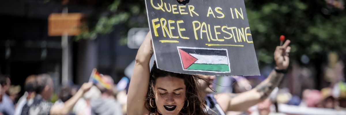A person holds a sign reading "Queer as in Free Palestine" at a Pride Parade.