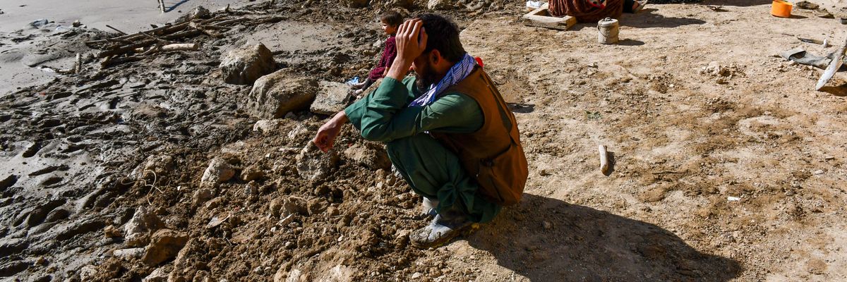 Afghan sits looking at flood damage.