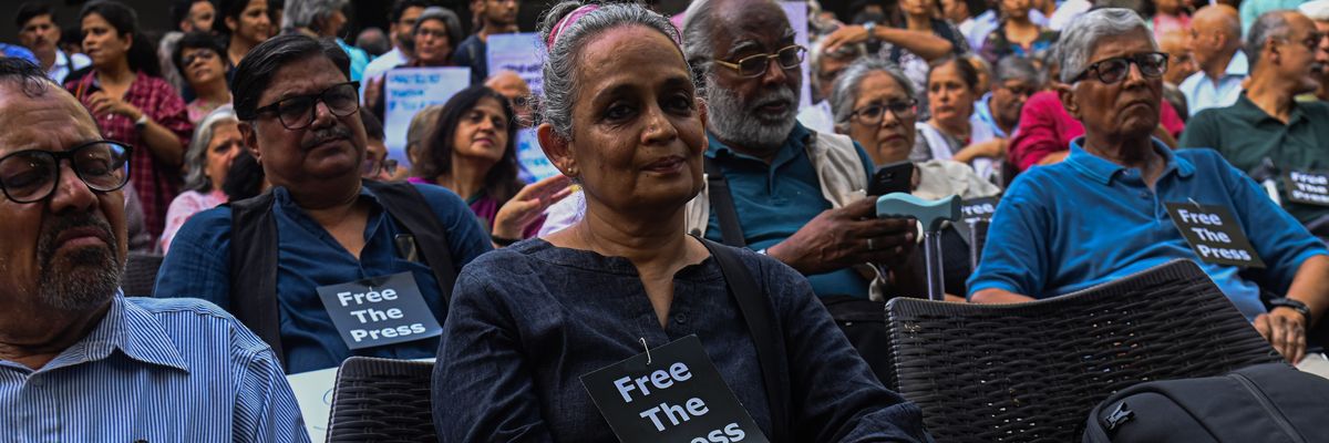 Arundhati Roy attends a demonstration wearing a small "Free the Press" sign.