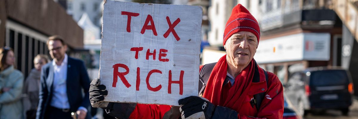 British millionaire, poses with a placard reading "Tax the rich"