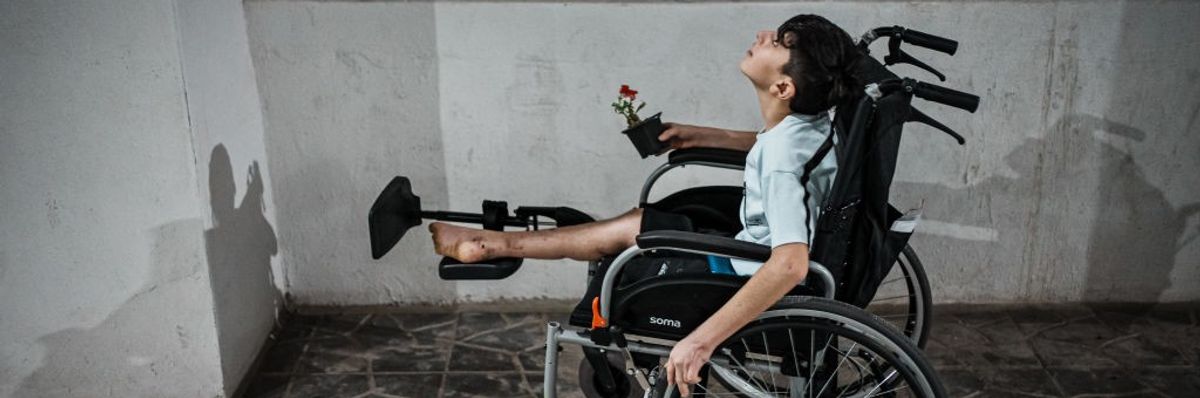 Gaza boy amputee in a wheelchair carrying a flower in a small pot 