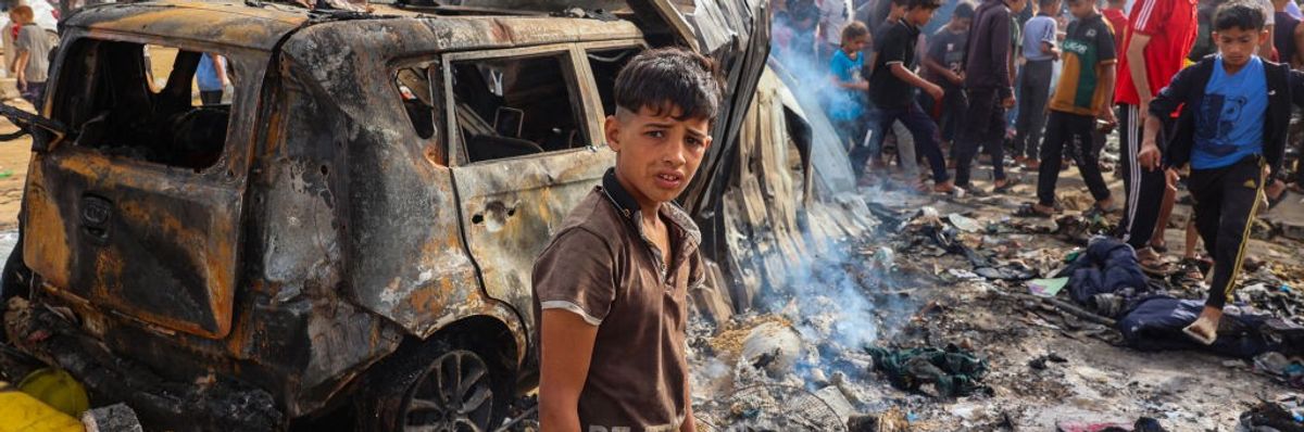 Palestinian boy standing in front of burned car 