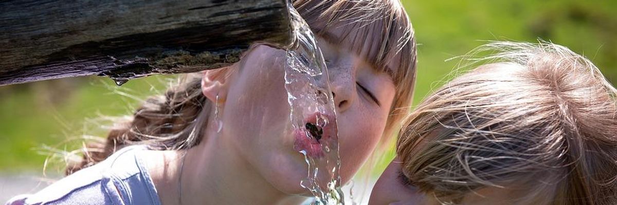 Two children drinking water outdoors. An estimated 110 million Americans are potentially exposed to 'forever chemicals' through drinking water.