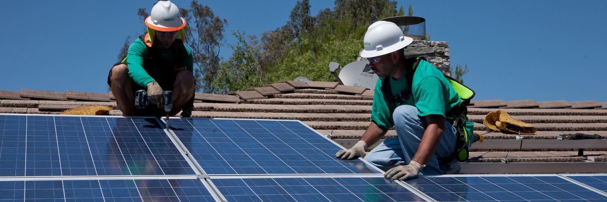 Two workers install solar panels on a home in Oak View, California.