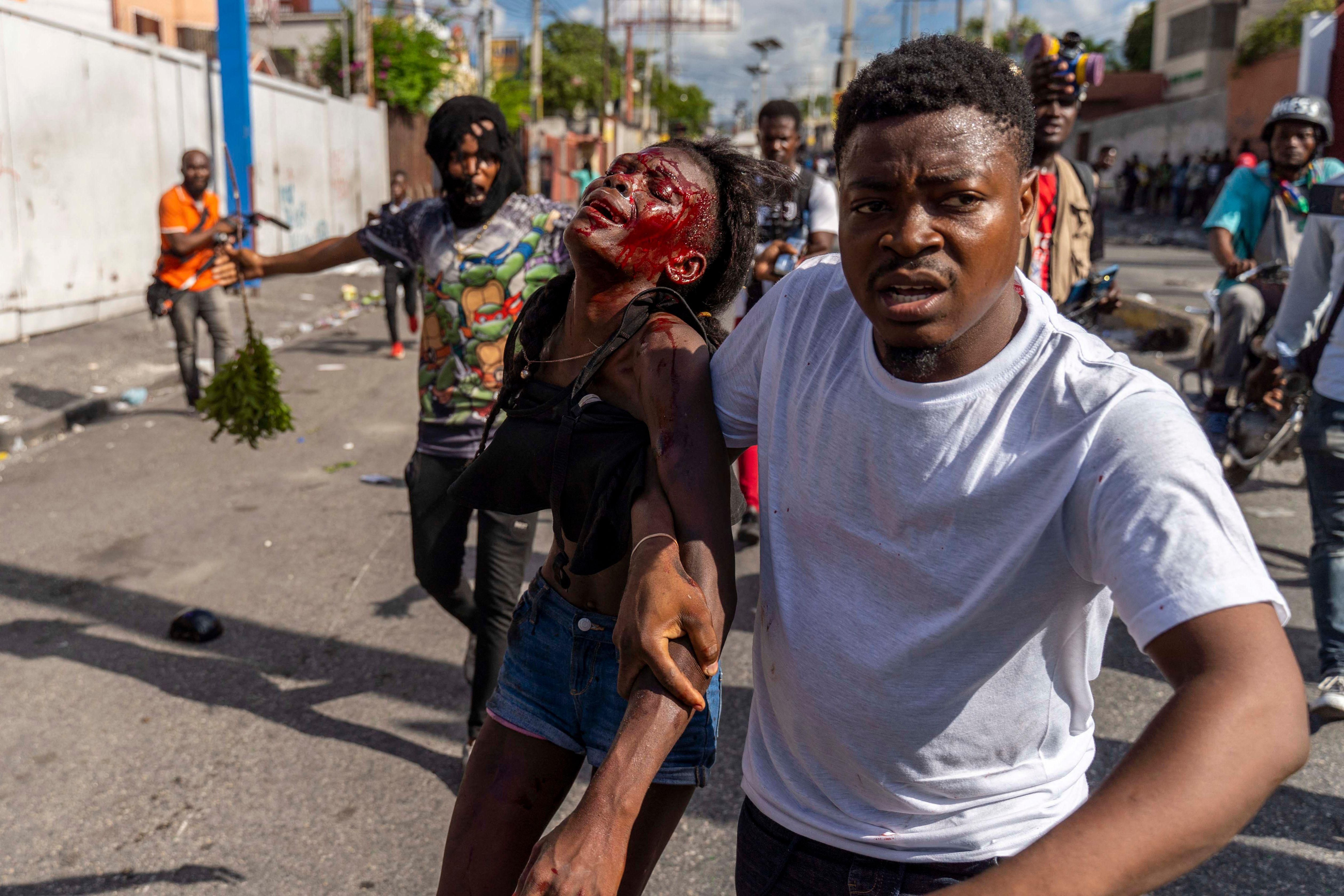 A man assists an injured woman during a protest demanding the resignation of Haitian Prime Minister Ariel Henry in Port-au-Prince, Haiti on October 10, 2022.