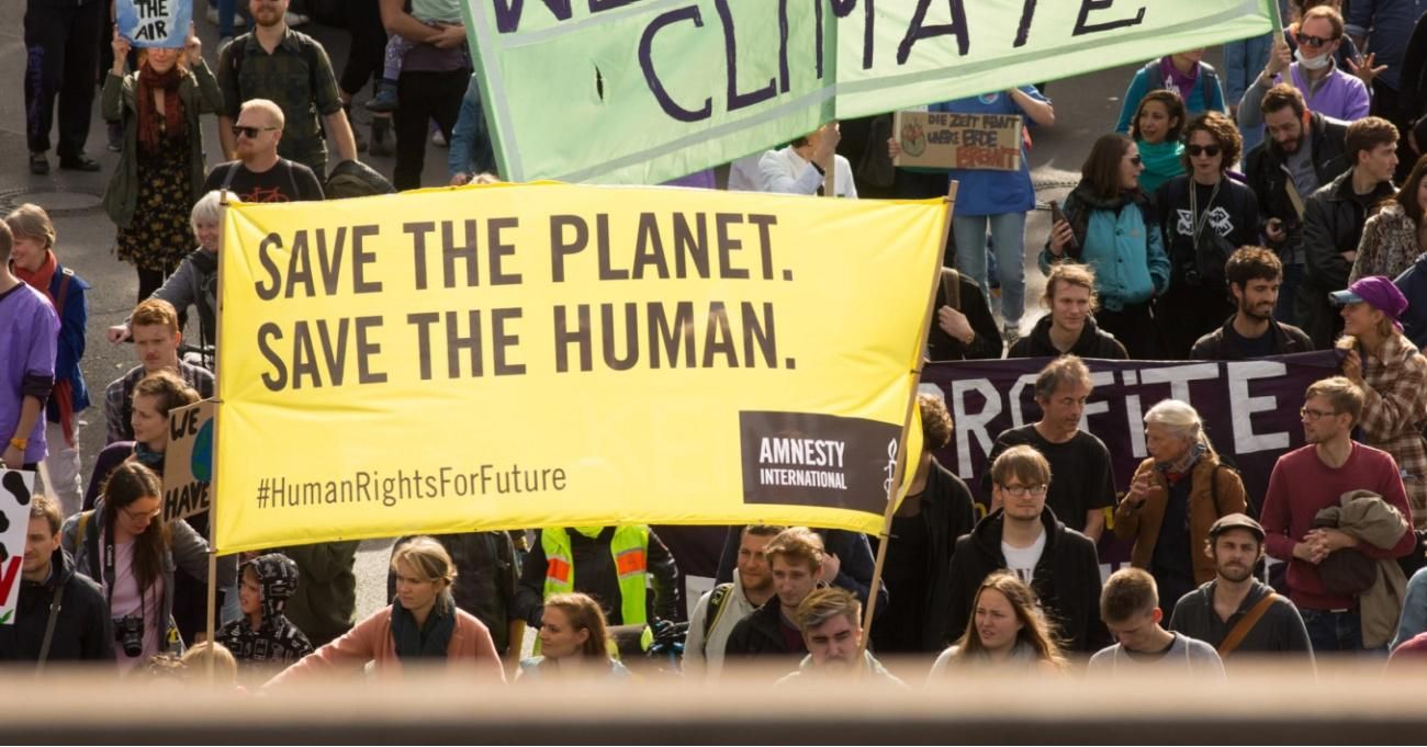 A protest sign reads "Save the Planet, Save the Human"